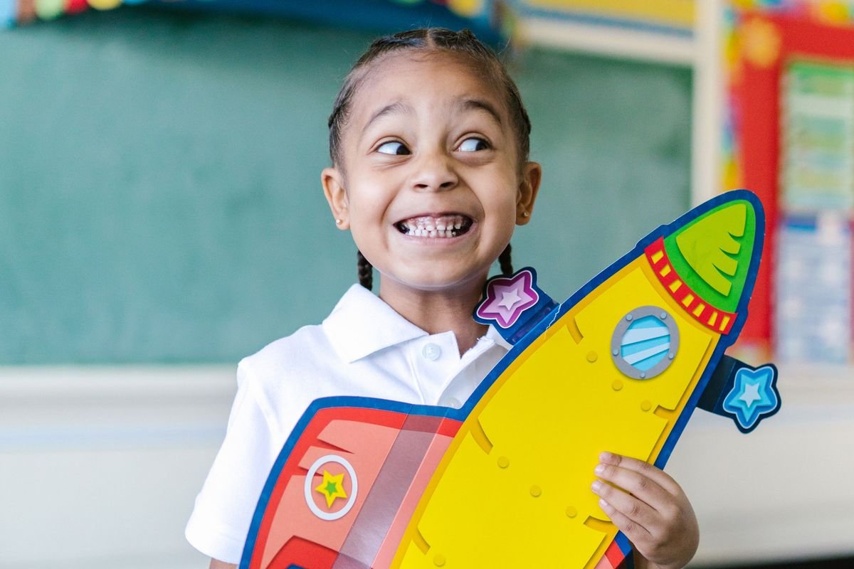 Beaming preschooler holding a paper rocket ship