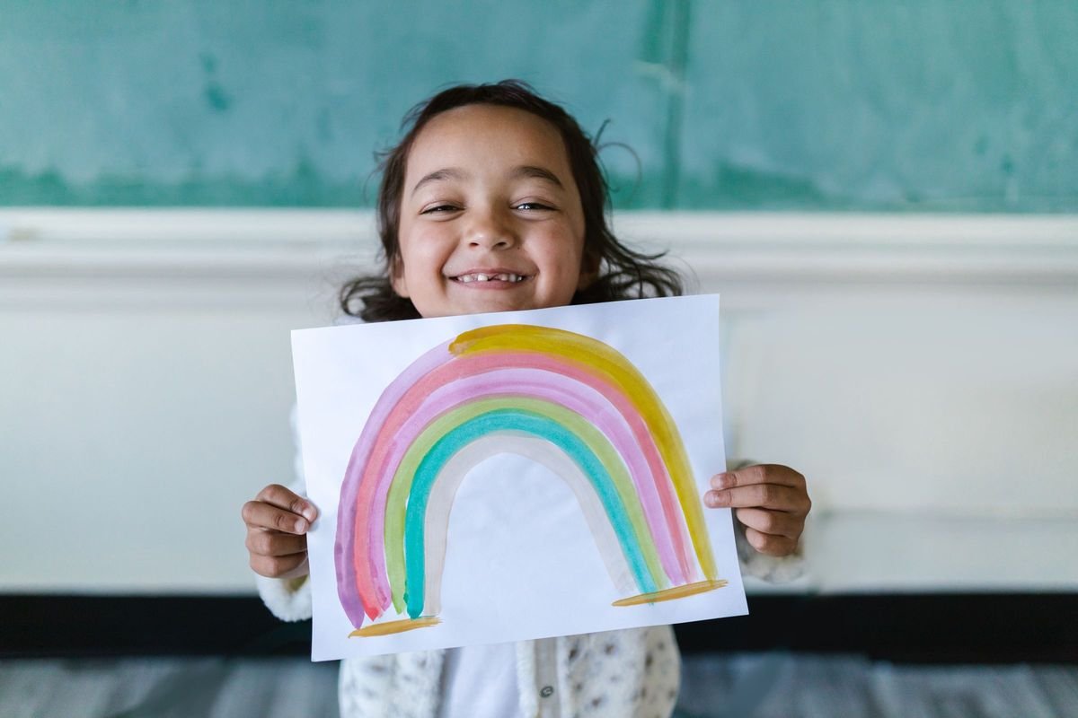 Smiling preschooler holding up a rainbow painting