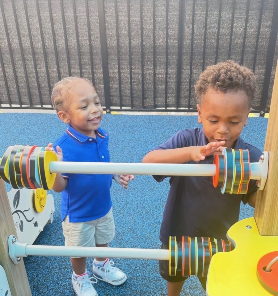Two preschoolers spinning colorful beads on the playground counting frame