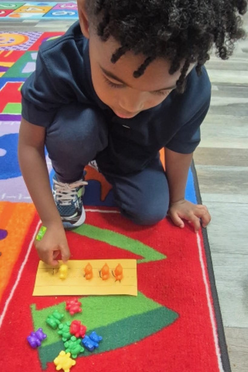 Preschooler placing counting bears on a letter card on the classroom rug