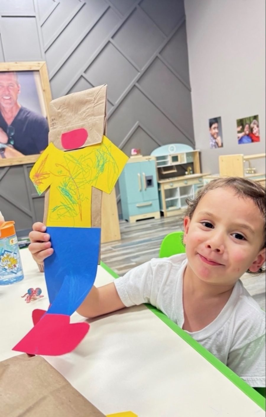 Preschooler proudly holding up a paper-bag puppet made in class