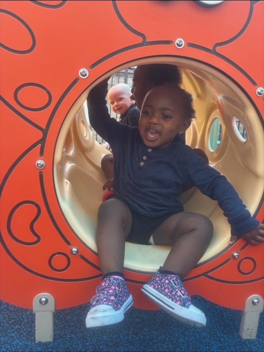 Laughing toddler sliding out of a playground tunnel