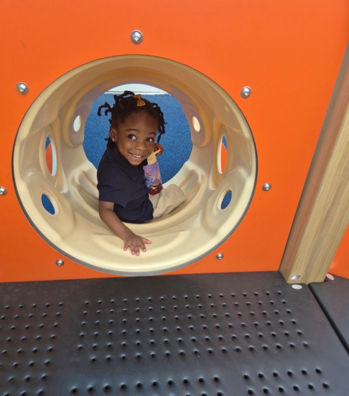 Smiling preschooler peeking out of a tunnel on the Expansion Academy playground