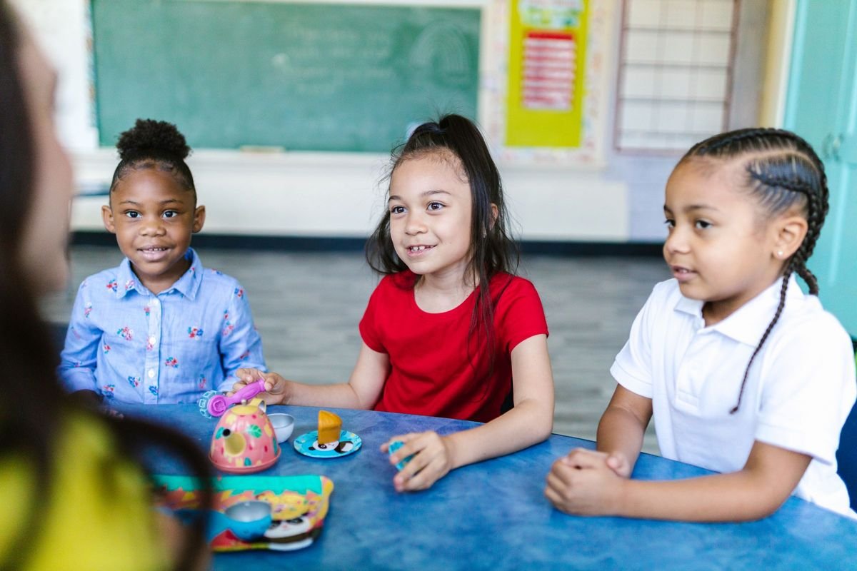 Three smiling preschoolers sitting together at a classroom table